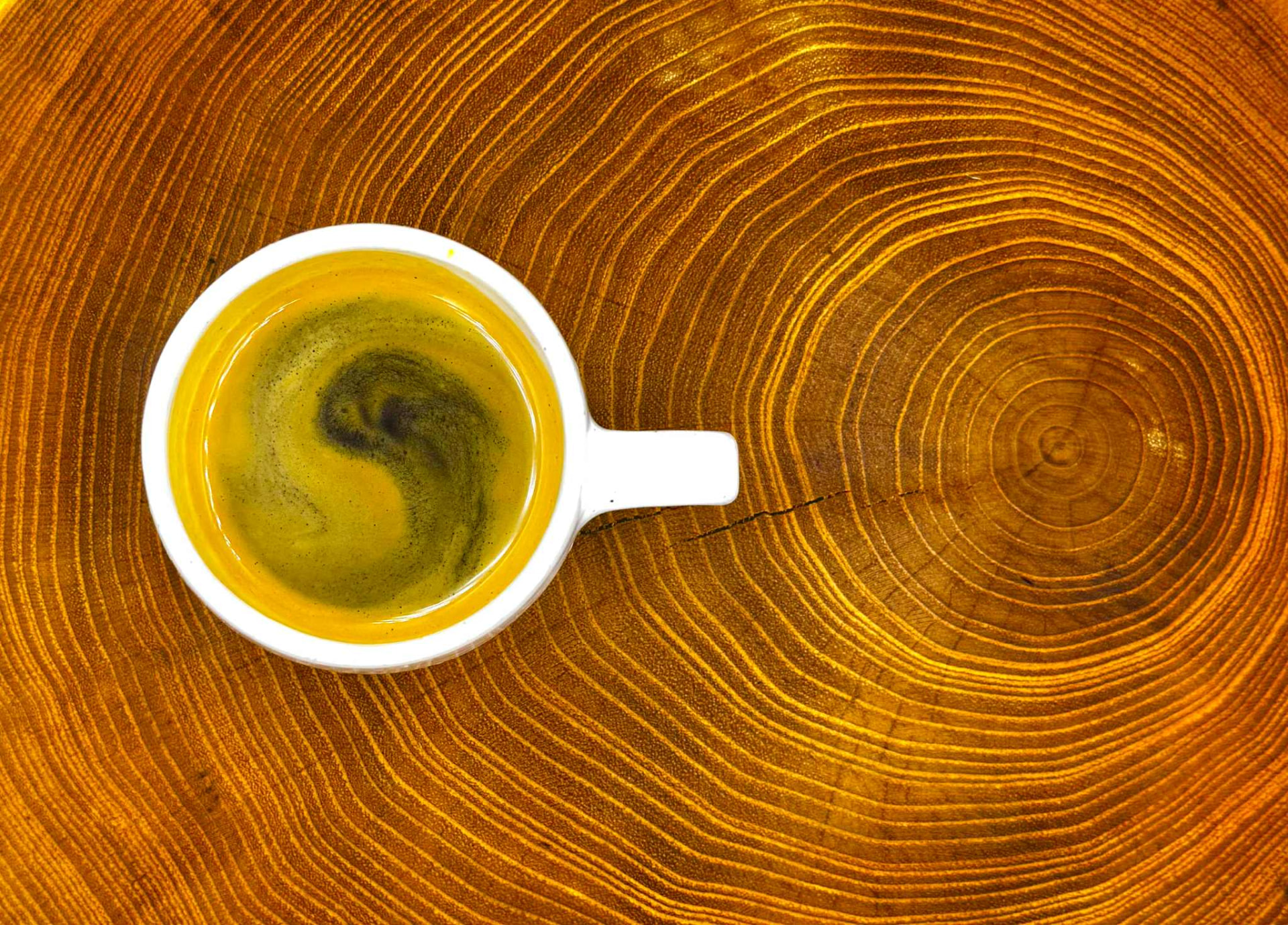 Espresso s crémou v bílém šálku na dřevěném špalku s letokruhy